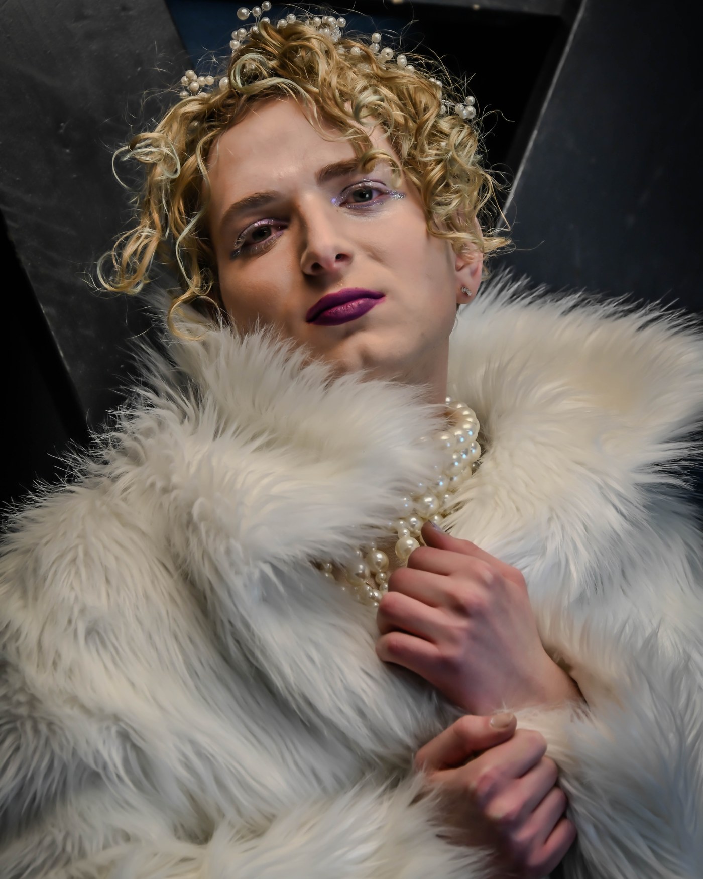 Iyal, the founder of TruBeauté, wearing a pearl crown and soft white fur, looking gently into the camera with editorial lighting.